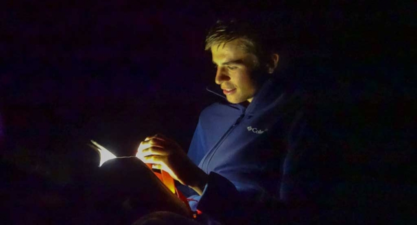 A person's face is illuminated by a flashlight as they read.